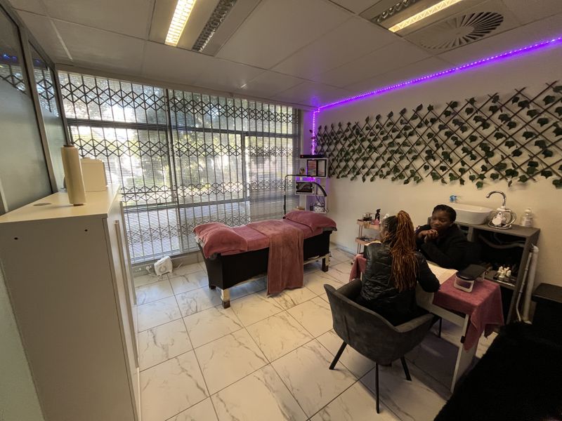 A functional office space featuring tiled flooring, a drop ceiling with recessed lighting, and a built-in sink area, currently utilized as a beauty treatment room.