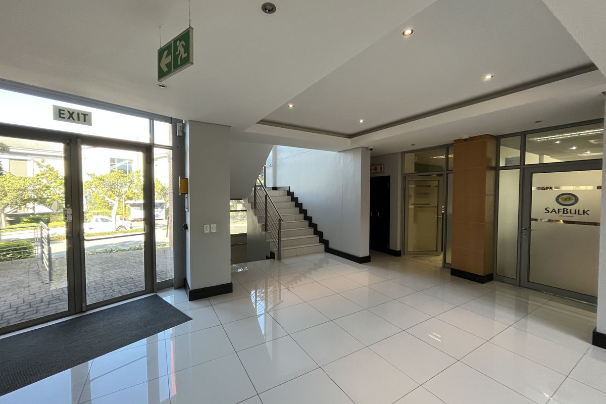 Modern office building entrance lobby featuring polished tiled flooring, recessed lighting, and a central staircase leading to upper levels.