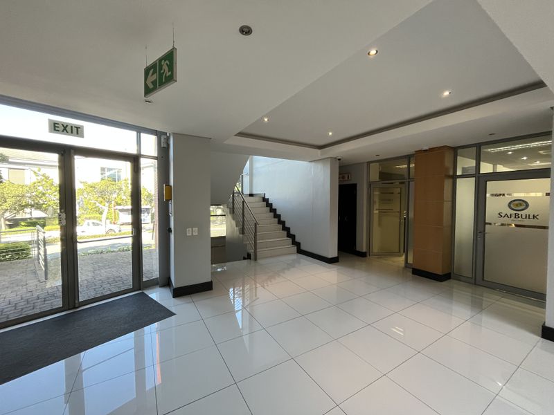 Modern office building entrance lobby featuring polished tiled flooring, recessed lighting, and a central staircase leading to upper levels.