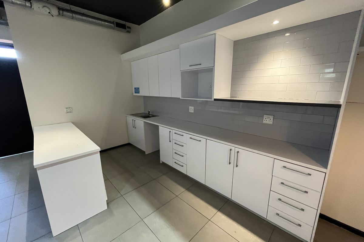 A modern, clean office kitchenette featuring white cabinetry, subway tile backsplash, stainless steel sink, and tiled flooring with an industrial exposed ceiling.