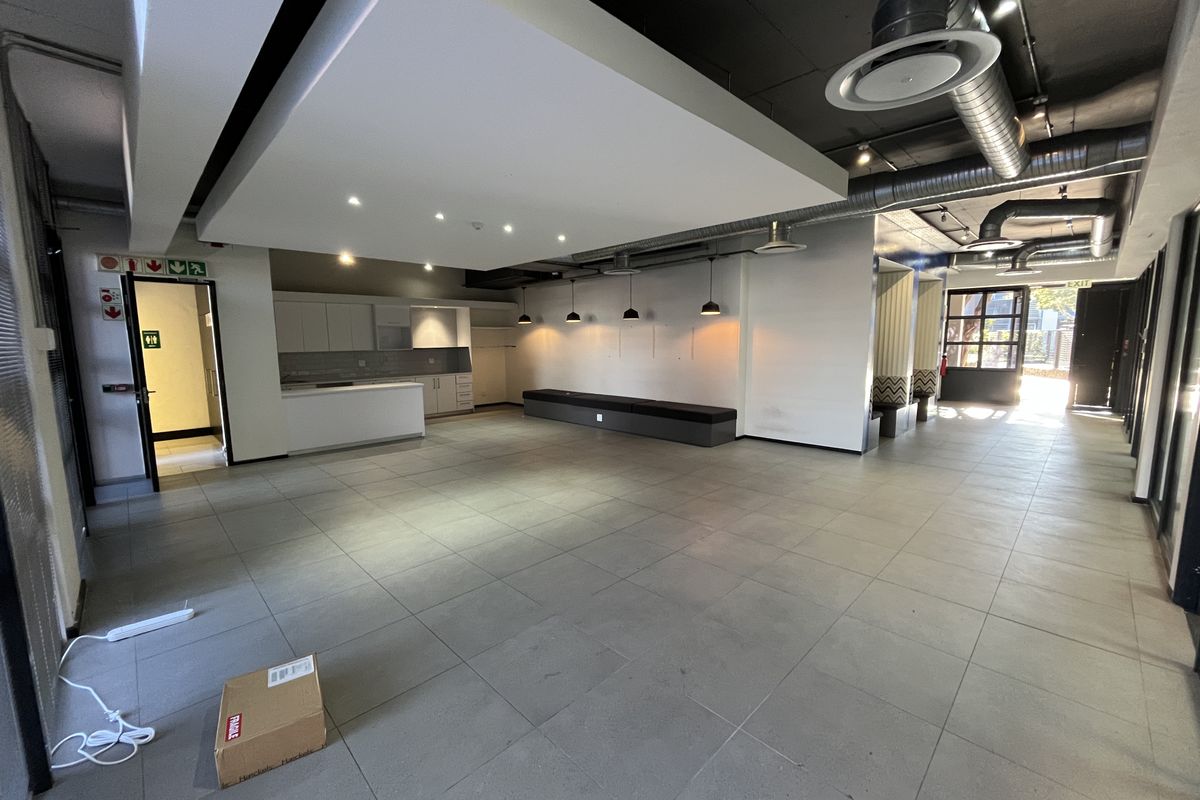 Spacious open-plan office area featuring modern tiled flooring, exposed industrial ducting, a built-in kitchenette, and integrated bench seating under a suspended ceiling feature.