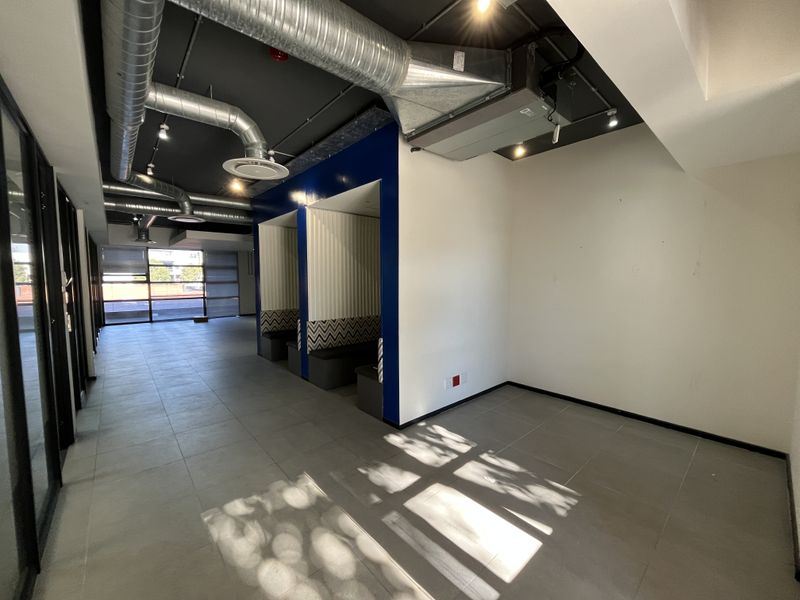 Modern open-plan office space featuring industrial-style exposed ductwork, tiled flooring, and built-in acoustic seating pods for collaborative work.
