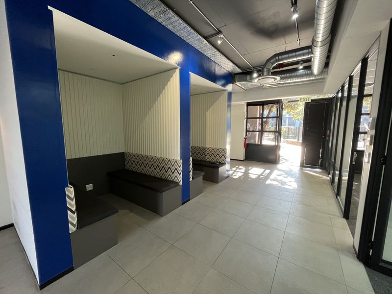 Modern office space featuring built-in acoustic seating booths, exposed industrial ceiling ductwork, and large glass partitions leading to an exterior exit.