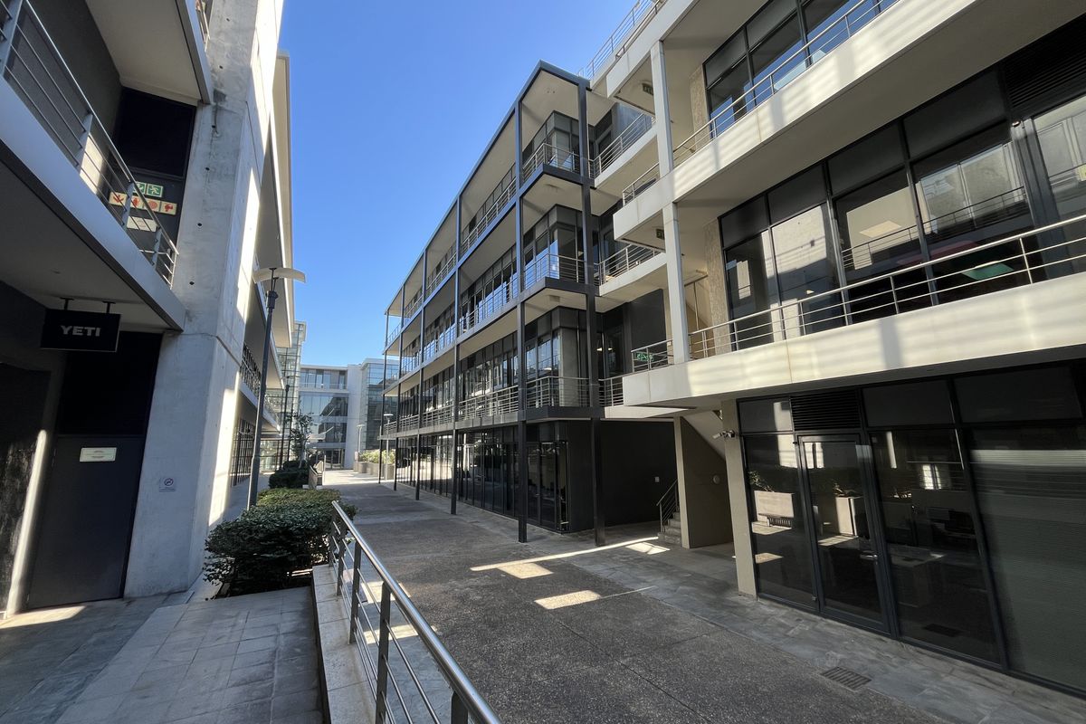 Modern multi-story office building exterior featuring contemporary glass facades, steel balcony railings, and a clean concrete pedestrian walkway between structures.