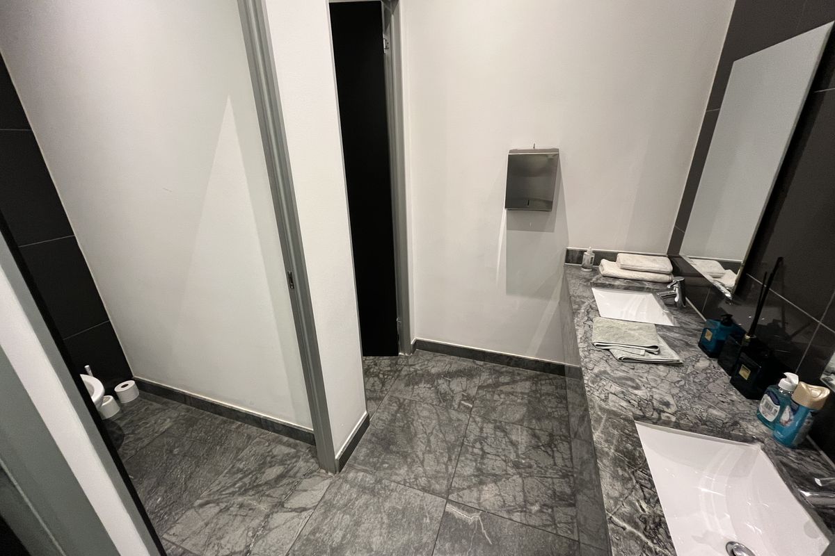 Modern office bathroom featuring a double vanity with marble countertop, undermount sinks, and contemporary dark tile flooring.