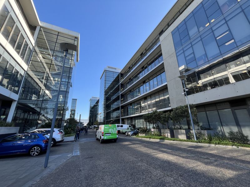 Modern multi-story office complex featuring extensive glass curtain wall facades and concrete structural elements with a paved access driveway.