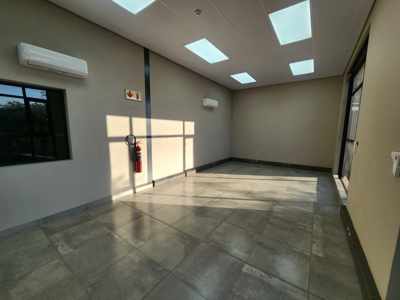 A clean, modern, and empty office space featuring tiled flooring, recessed ceiling lighting, and dual split-system air conditioning units.