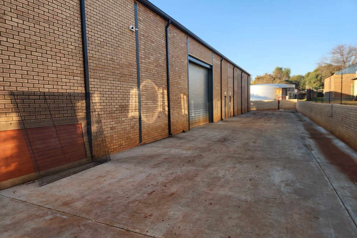 Rear exterior view of an industrial property featuring a face brick facade, concrete yard space, and a secure roller shutter door access point.
