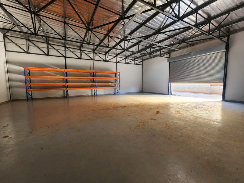Spacious industrial warehouse unit featuring high exposed steel roof trusses, durable concrete flooring, and a large roller shutter door for easy access.