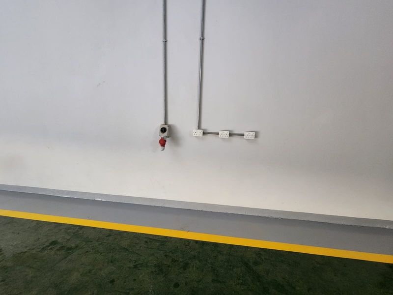 Industrial utility space featuring exposed electrical conduit, power sockets, and a painted concrete floor with safety markings.
