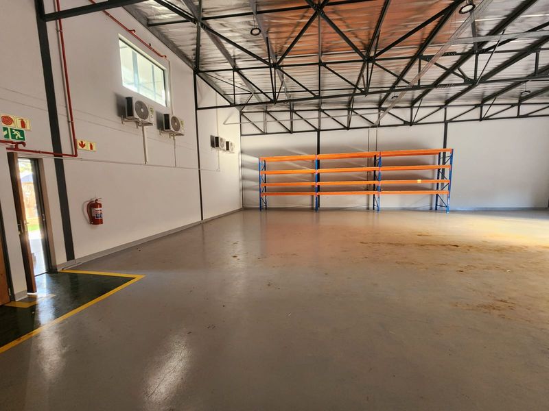 Spacious industrial warehouse unit featuring high exposed steel roof trusses, durable epoxy-coated flooring, wall-mounted air conditioning units, and integrated industrial shelving.