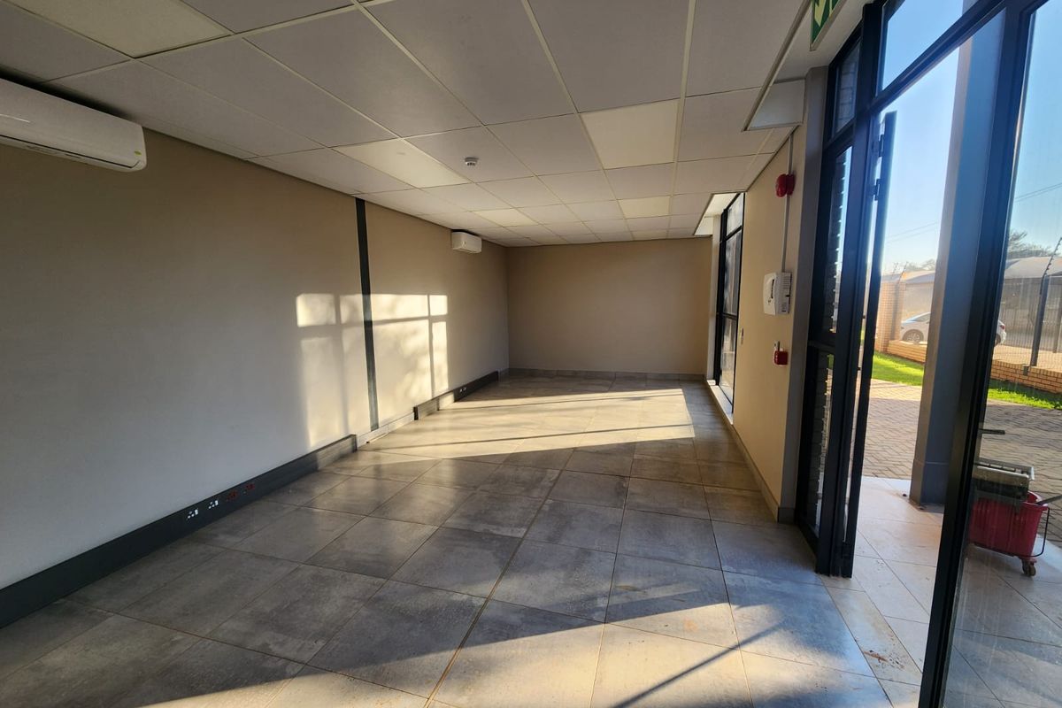 A bright, vacant office space featuring tiled flooring, a suspended ceiling, and dual split-system air conditioning units with direct access to the exterior.