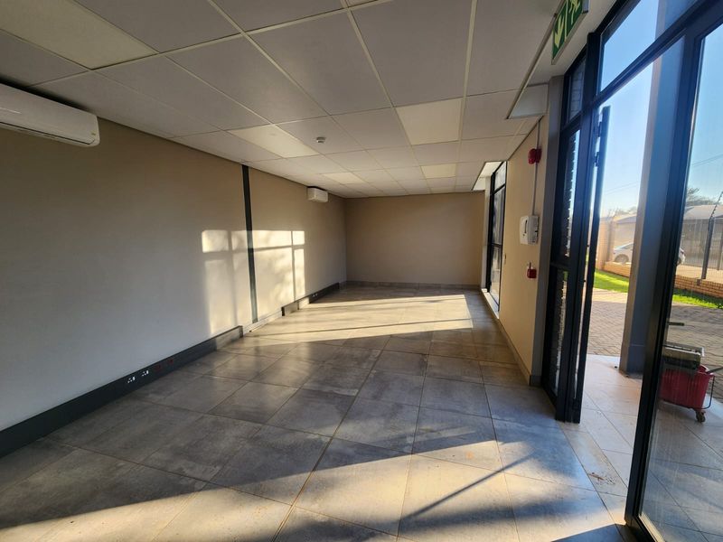A bright, vacant office space featuring tiled flooring, a suspended ceiling, and dual split-system air conditioning units with direct access to the exterior.