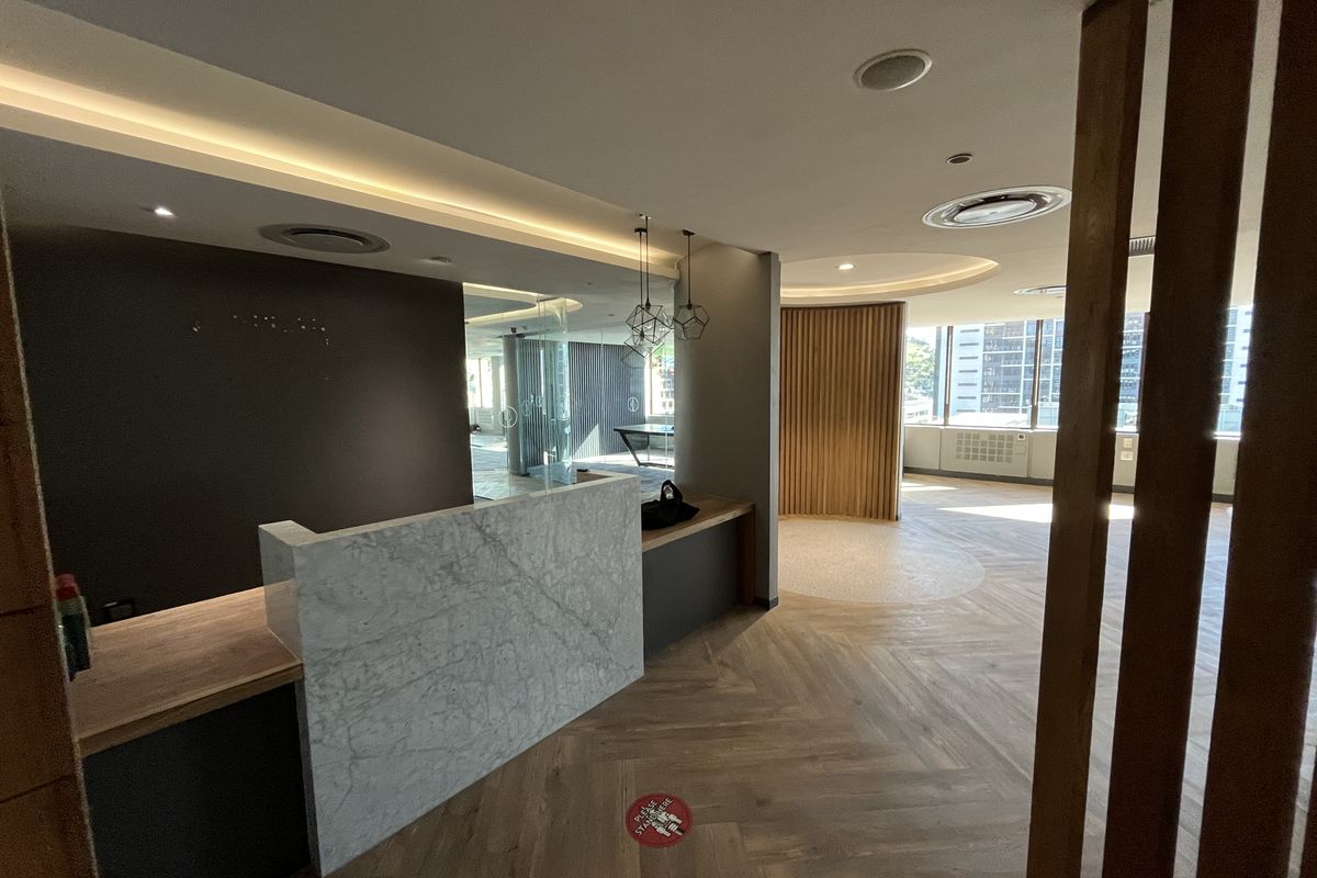 Modern office reception area featuring a marble desk, herringbone timber flooring, and elegant timber slat accents with recessed ceiling lighting.