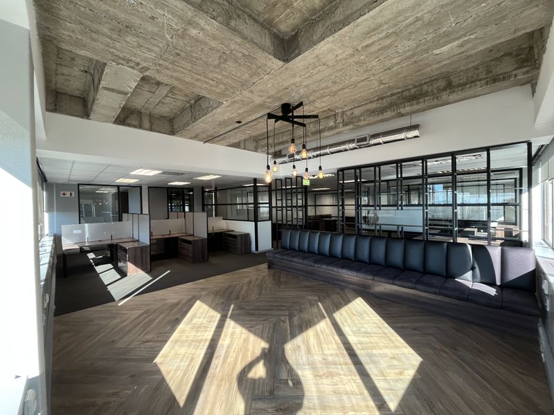 Modern open-plan office space featuring exposed concrete ceilings, herringbone wood flooring, integrated bench seating, and stylish glass partition walls for a professional aesthetic.