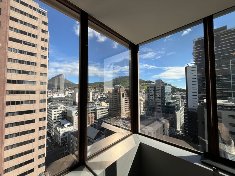 A high-rise office space featuring expansive floor-to-ceiling corner windows with panoramic views of the city skyline and surrounding mountains.