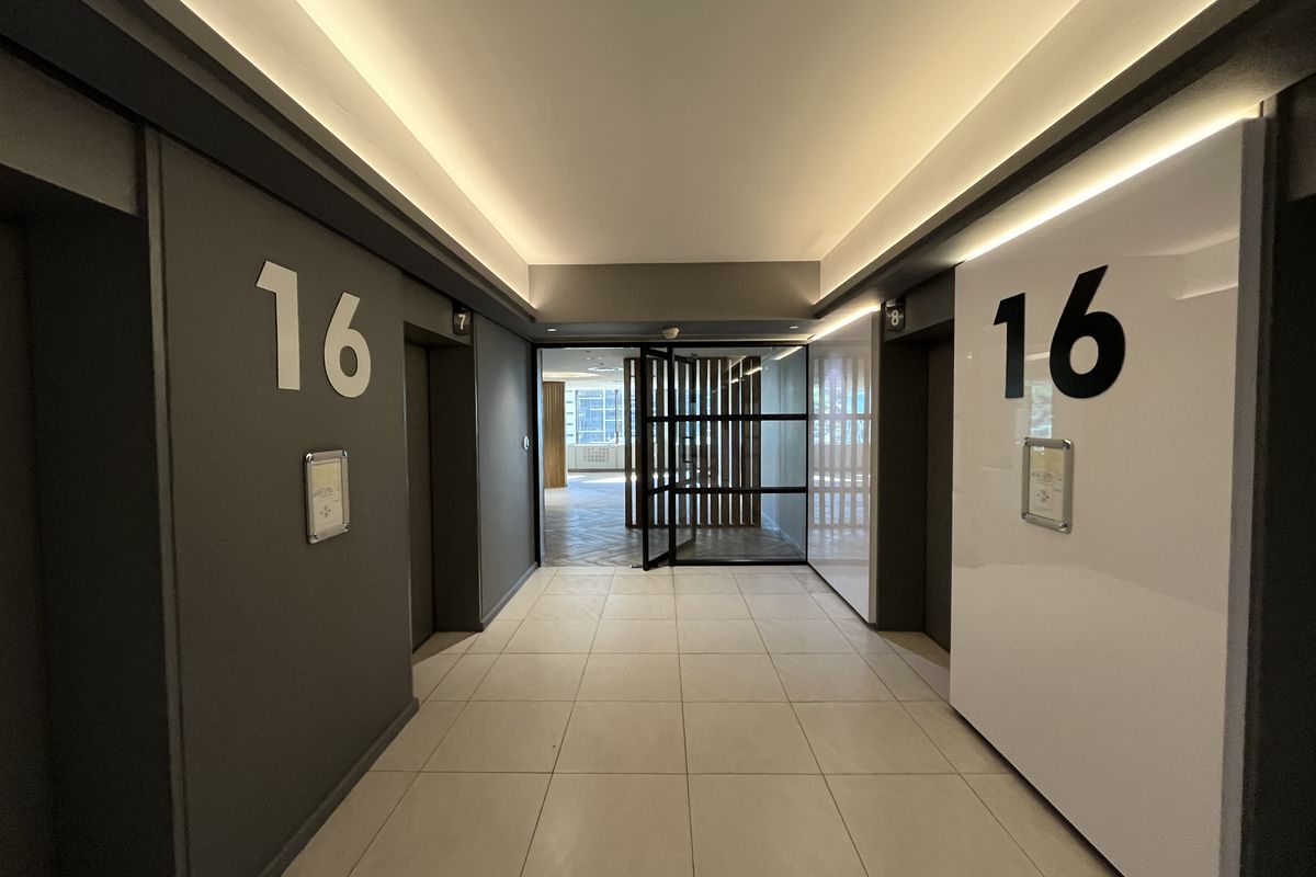 Modern office building elevator lobby on the 16th floor featuring tiled flooring, recessed cove lighting, and a glass partition door leading to the office space.