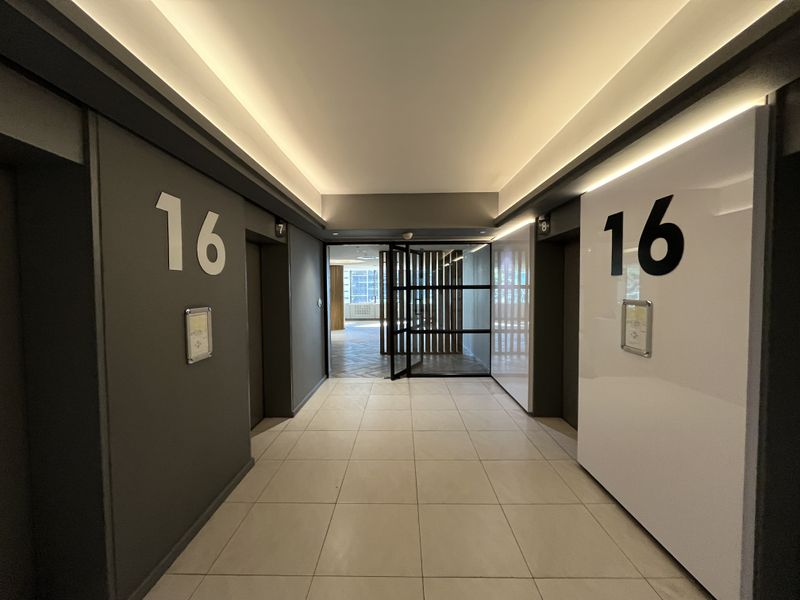 Modern office building elevator lobby on the 16th floor featuring tiled flooring, recessed cove lighting, and a glass partition door leading to the office space.