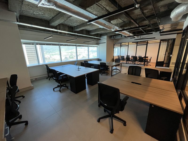 Modern open-plan office space featuring an industrial-style exposed concrete ceiling, large windows with city views, and glass-partitioned meeting rooms.