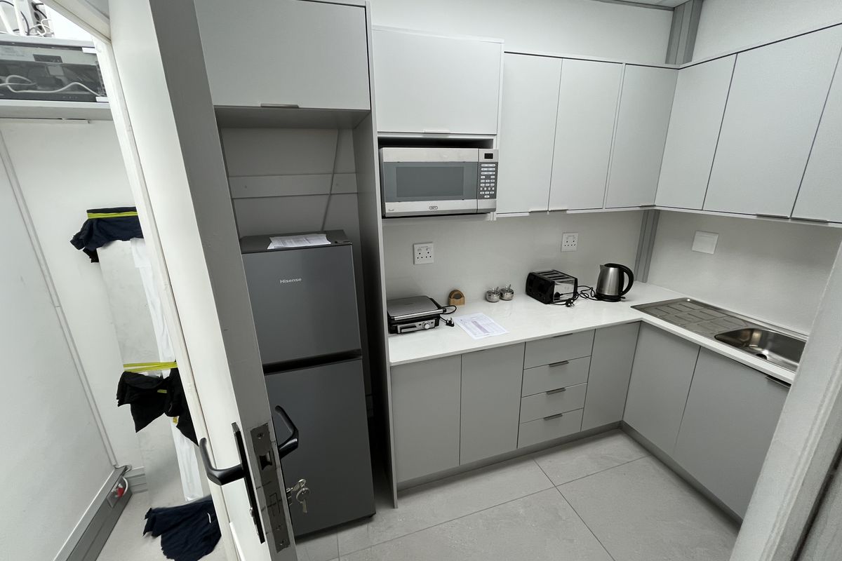 A compact, modern office kitchenette featuring grey cabinetry, a built-in microwave, stainless steel sink, and clean tiled flooring.