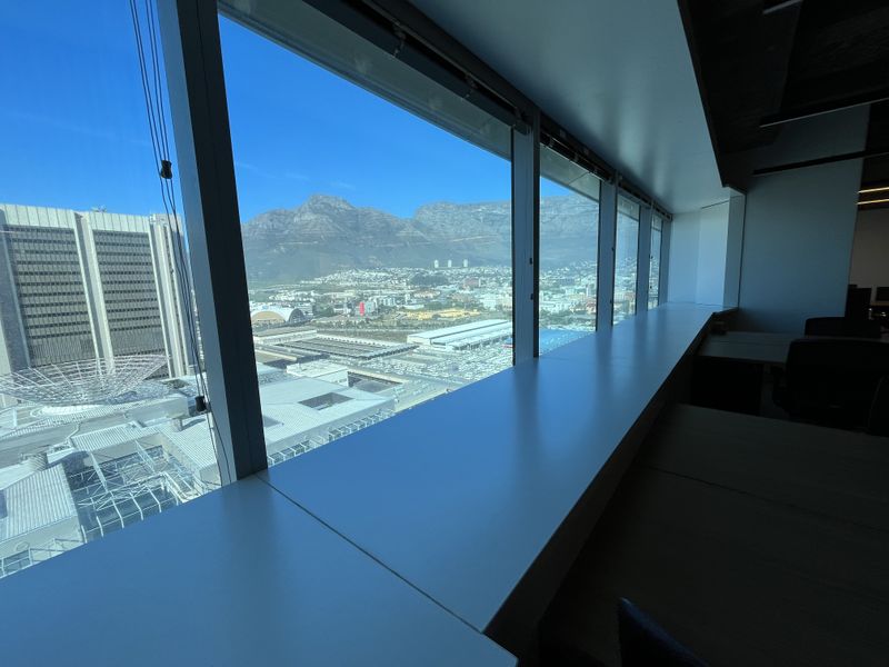 Modern office space featuring expansive floor-to-ceiling windows with panoramic mountain and city views and a functional built-in window ledge.