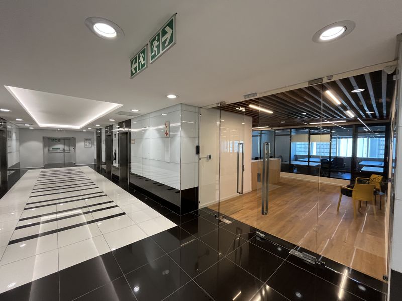 Modern office lobby featuring high-gloss tiled flooring, glass partitions, and a professional reception area with timber flooring and recessed lighting.