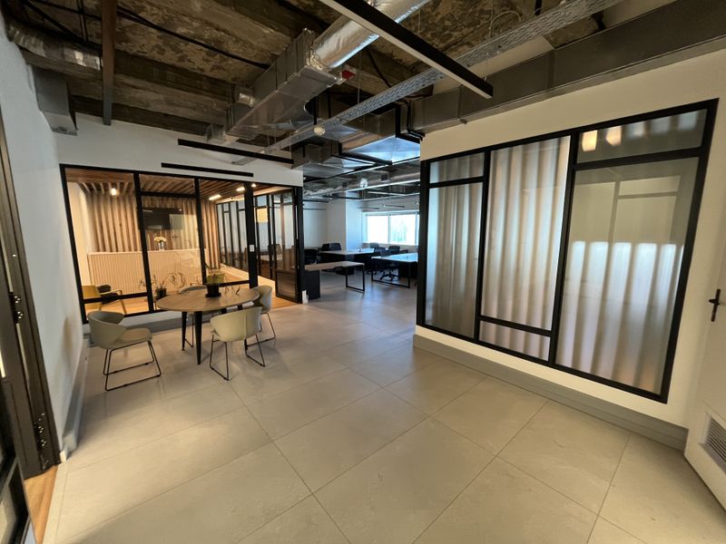 Modern open-plan office space featuring industrial-style exposed ceilings, glass partition walls, and large format floor tiles.