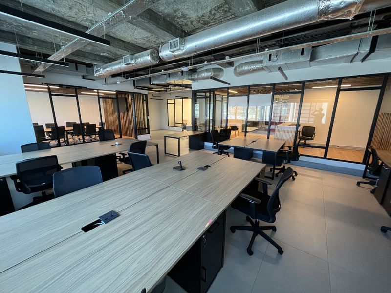 Modern open-plan office space featuring exposed industrial ceilings, glass-partitioned meeting rooms, and contemporary tiled flooring with integrated workstation power connectivity.
