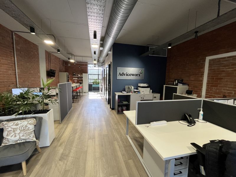 Modern open-plan office space featuring exposed brick walls, industrial-style exposed ducting, and contemporary laminate flooring with integrated workstation areas.