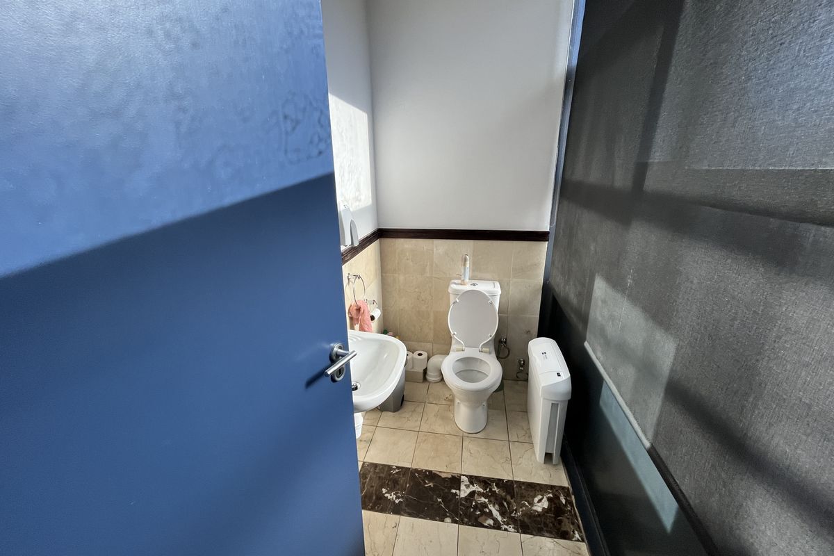 A functional office bathroom featuring a pedestal basin, toilet, and tiled flooring with decorative border accents.