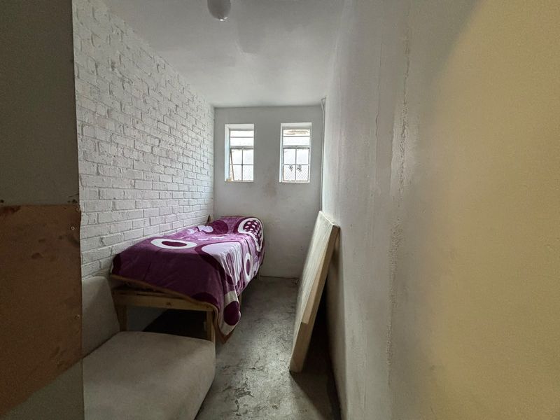 A small, industrial-style bedroom featuring an exposed white brick wall, concrete flooring, and two small casement windows.