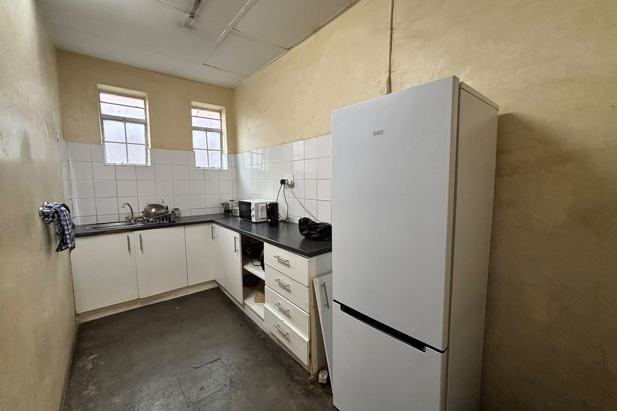 A functional industrial kitchen space featuring white cabinetry, laminate countertops, tiled splashbacks, and a drop ceiling, requiring cosmetic updates to improve overall condition.