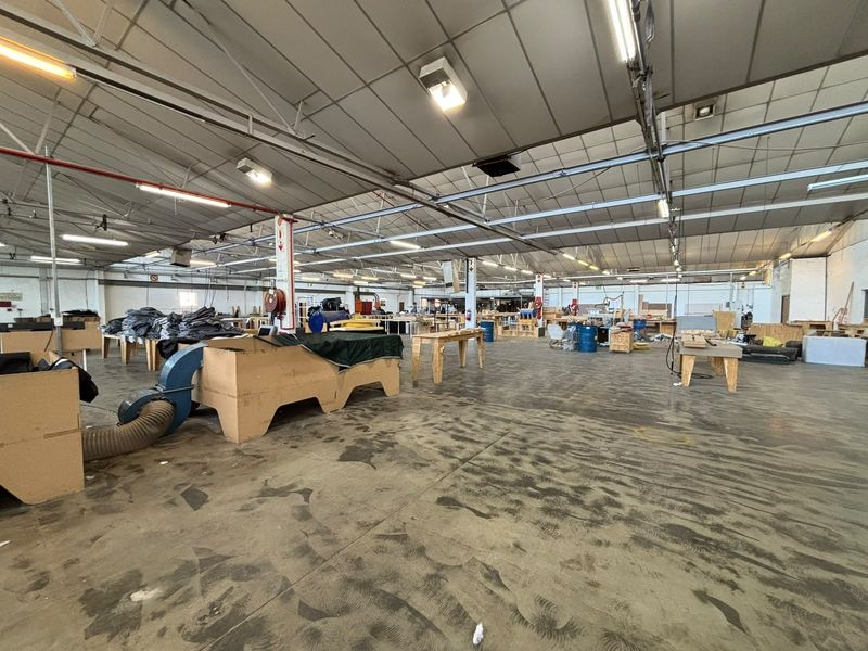 Spacious industrial warehouse area featuring high exposed steel truss ceilings, durable concrete flooring, and integrated industrial lighting and ventilation systems.