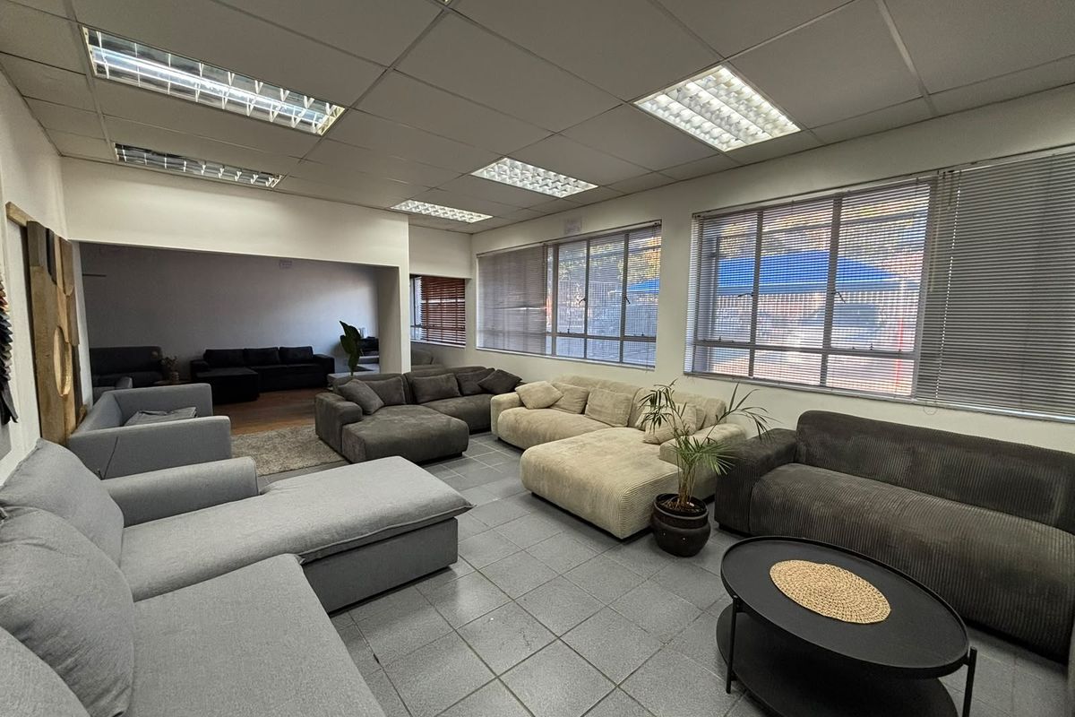 Spacious industrial-style living area featuring tiled flooring, suspended ceiling with recessed lighting, and large windows with venetian blinds.