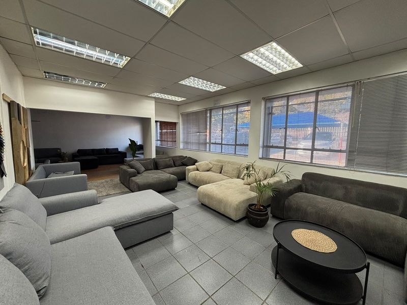 Spacious industrial-style living area featuring tiled flooring, suspended ceiling with recessed lighting, and large windows with venetian blinds.