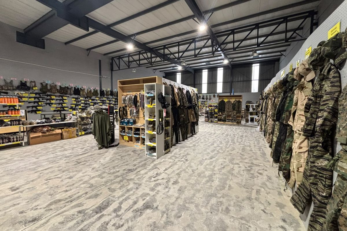 Spacious industrial warehouse unit featuring exposed steel roof trusses, polished concrete flooring, and extensive built-in wall shelving for retail or storage use.