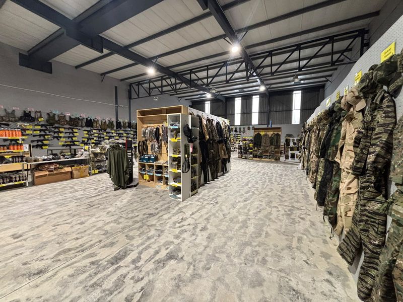 Spacious industrial warehouse unit featuring exposed steel roof trusses, polished concrete flooring, and extensive built-in wall shelving for retail or storage use.