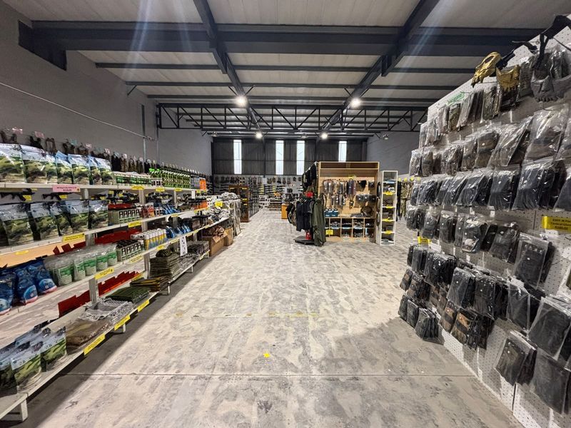 Spacious industrial warehouse interior featuring exposed steel roof trusses, polished concrete flooring, and extensive wall-mounted retail display shelving.