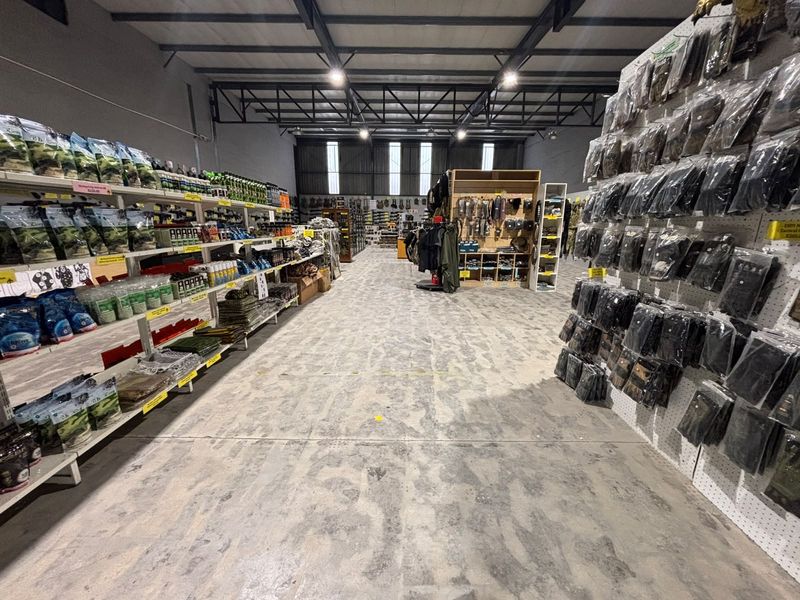 Spacious industrial warehouse unit featuring exposed steel roof trusses, polished concrete flooring, and high-bay lighting, currently utilized as a retail display area.