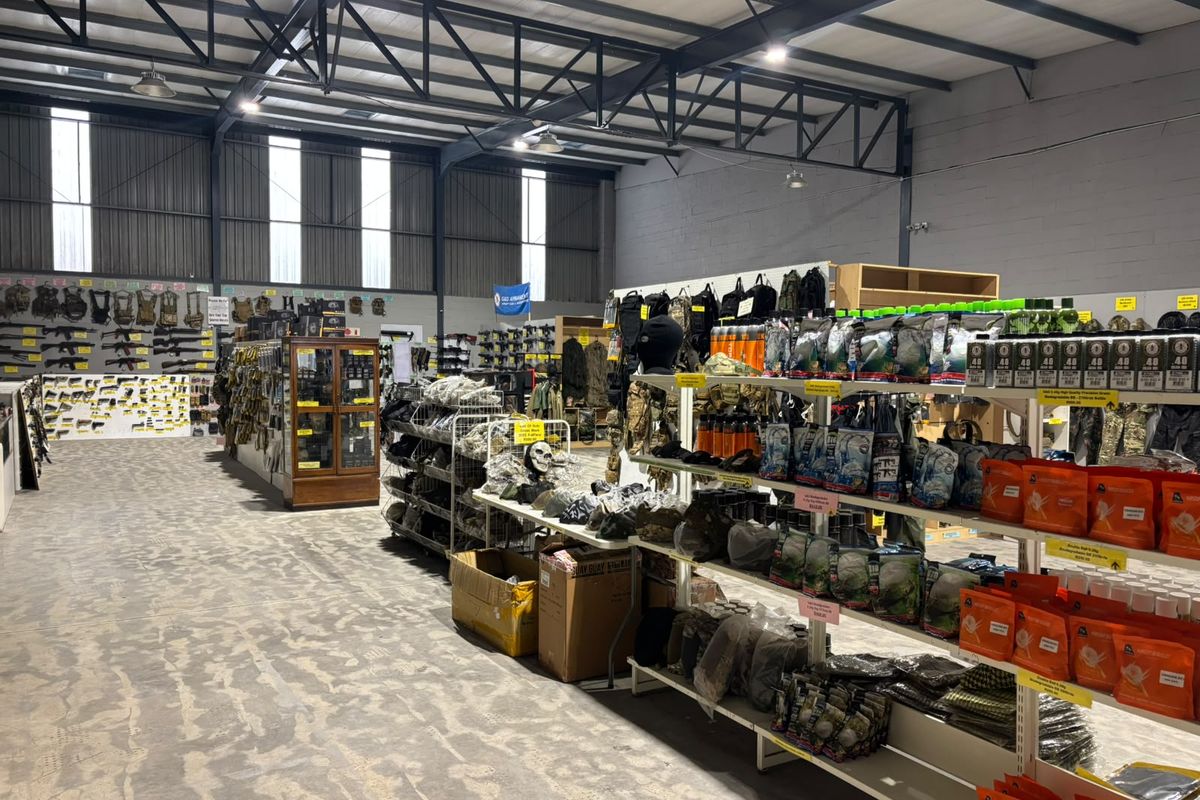 Spacious industrial warehouse interior featuring exposed steel roof trusses, high-bay lighting, and durable concrete flooring, currently utilized as a retail display area.