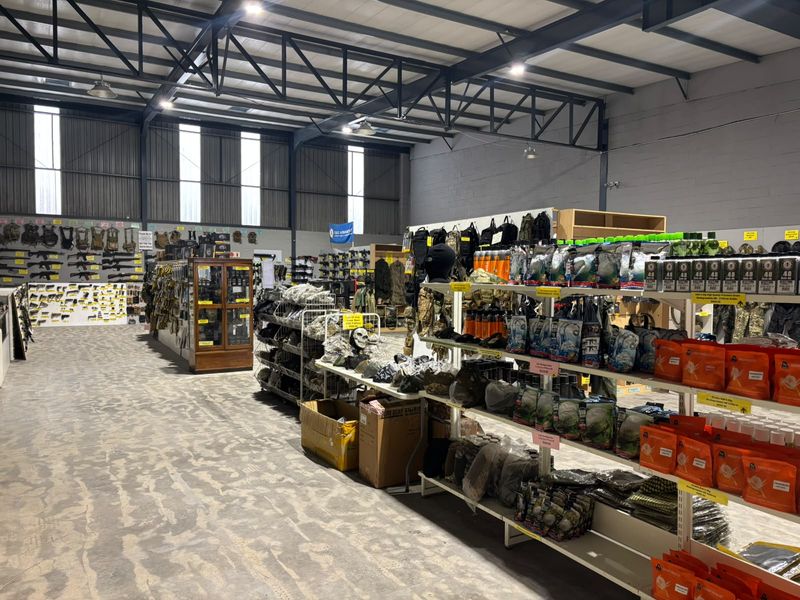 Spacious industrial warehouse interior featuring exposed steel roof trusses, high-bay lighting, and durable concrete flooring, currently utilized as a retail display area.