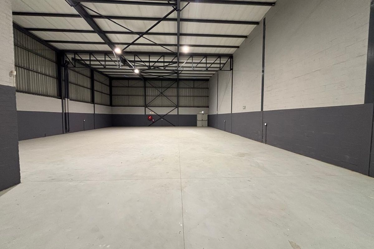 A spacious, clean industrial warehouse unit featuring high ceilings with exposed steel trusses, concrete flooring, and freshly painted masonry walls.
