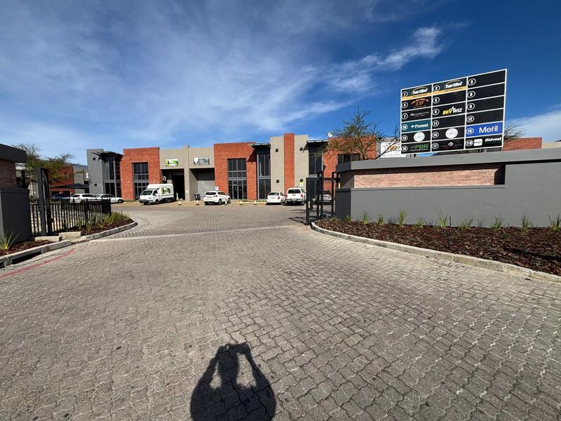 Front view of a modern industrial business park featuring a paved entrance, brick facade, and a prominent tenant directory signage board.