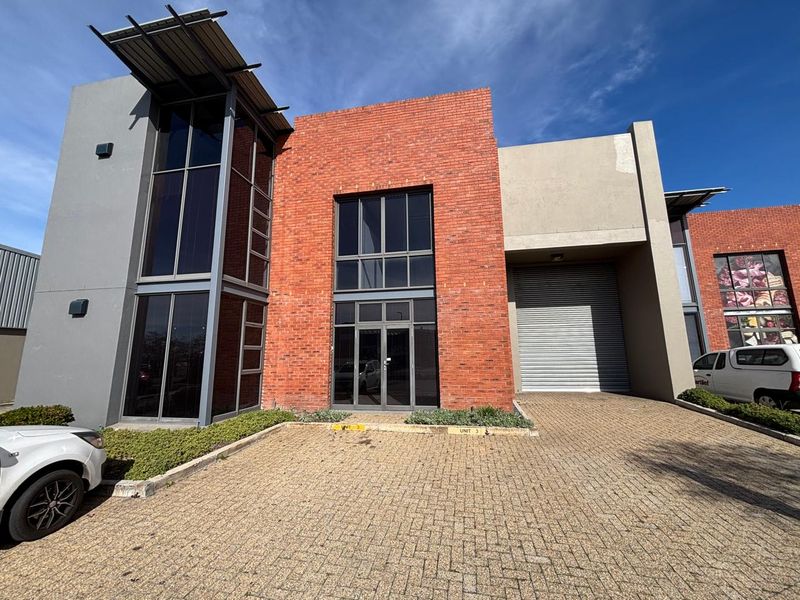 Modern industrial unit featuring a striking red brick facade, large glass windows, and a functional roller shutter door with a paved driveway entrance.