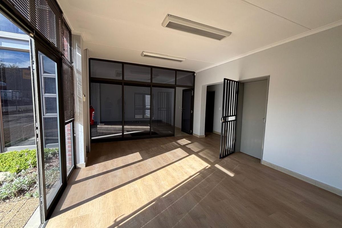 A bright, open-plan office space featuring modern laminate flooring, large glass partitions, and secure access points, suitable for a professional work environment.