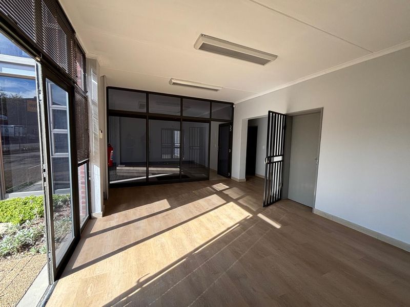 A bright, open-plan office space featuring modern laminate flooring, large glass partitions, and secure access points, suitable for a professional work environment.