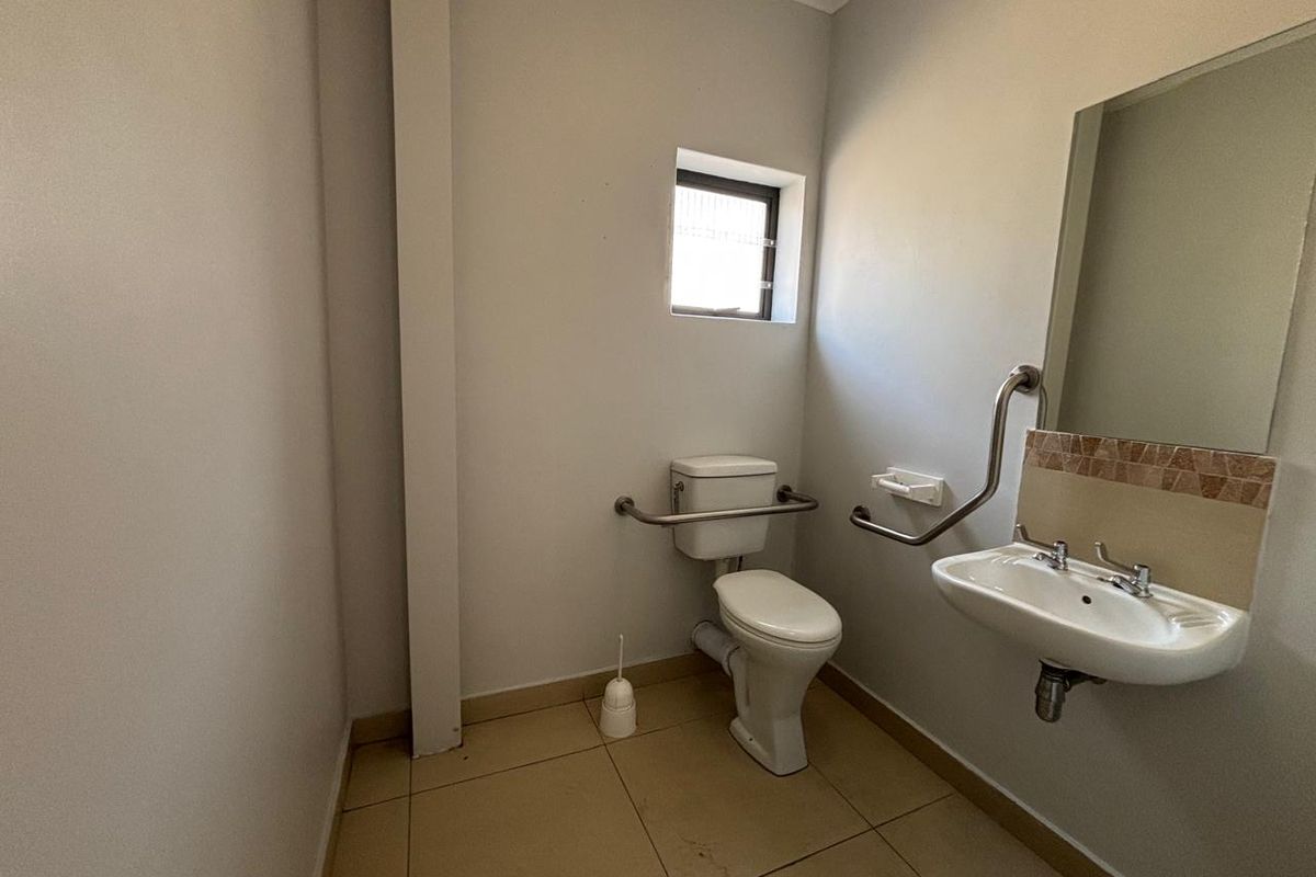 A functional, accessible bathroom featuring a toilet, wall-mounted basin, grab rails, and tiled flooring.