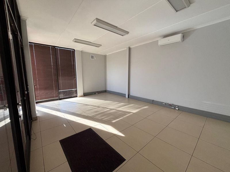A bright, vacant office space featuring tiled flooring, split-system air conditioning, and large sliding glass doors with venetian blinds.