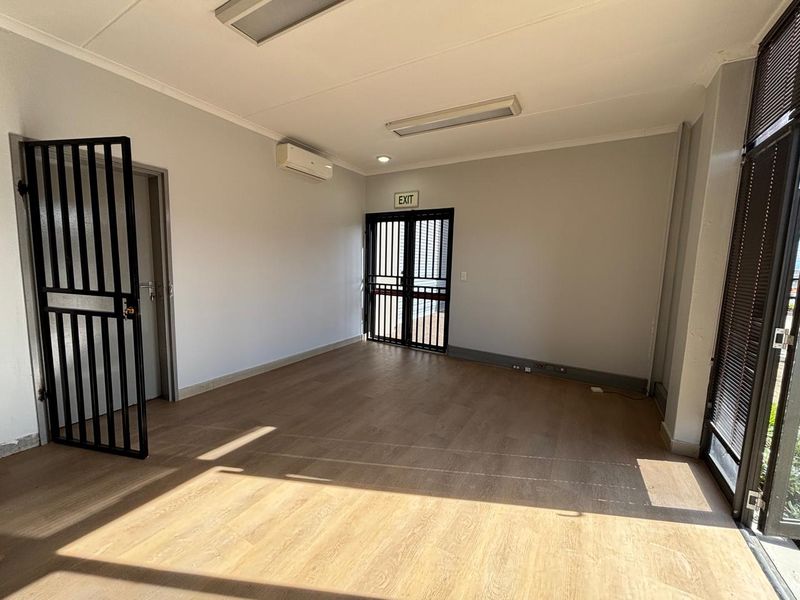 A bright, empty office space featuring laminate flooring, a split-system air conditioner, and secure access points.