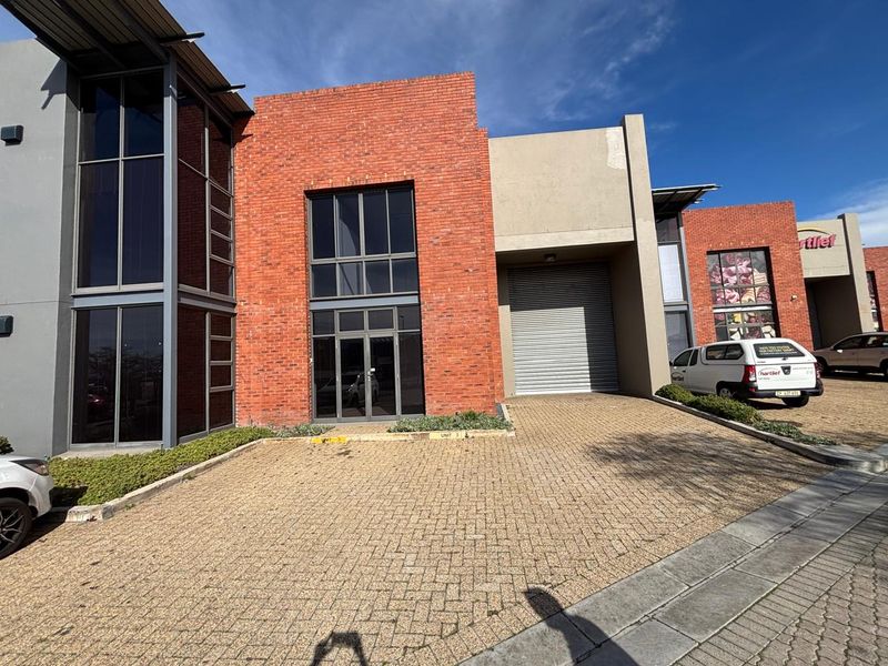 Front elevation of an industrial unit featuring a brick facade, large glass windows, and a roller shutter door with a paved driveway.